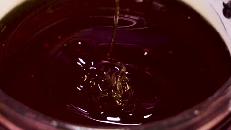 thick dark honey drizzling back into container, extreme closeup