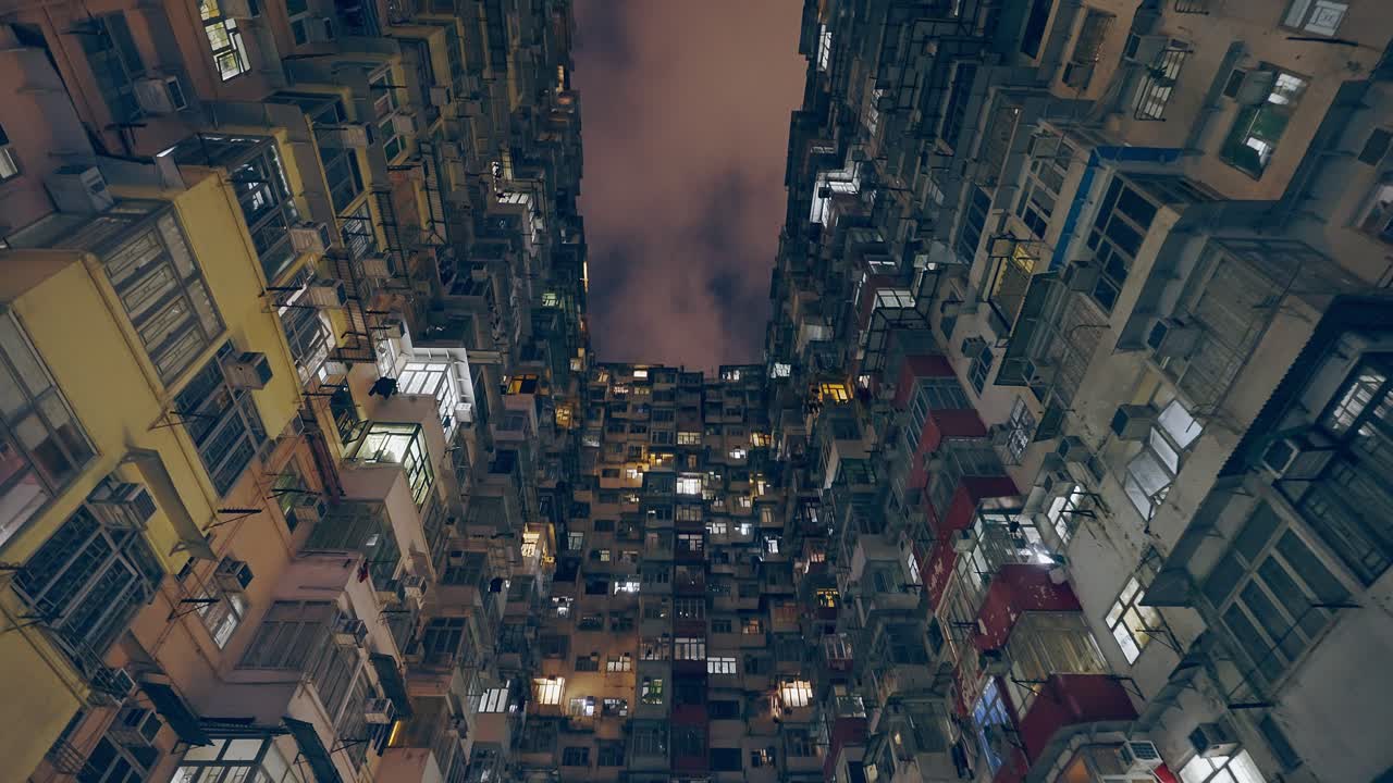 toma cinematográfica de un antiguo edificio de viviendas durante la noche, algunas ventanas todavía tienen luz abierta