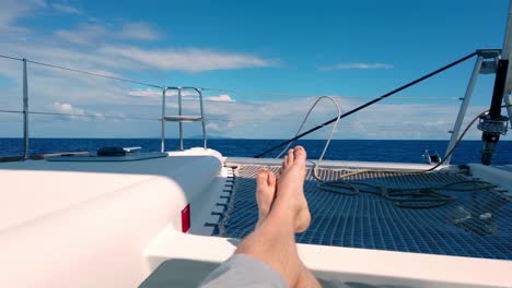 Legs-point-of-view-of-man-lay-down-enjoying-the-travel-on-a-beautiful-sailboat-yacht-with-the-ocean-around