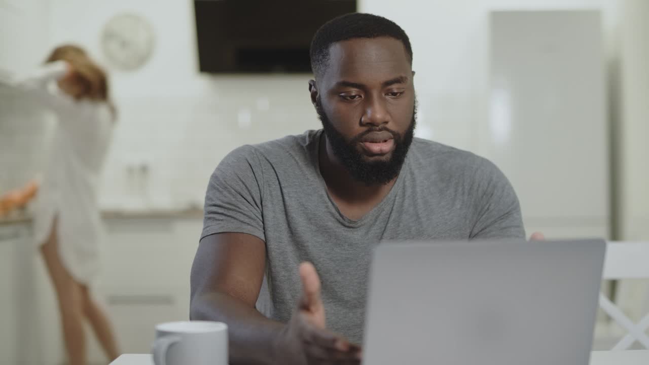 Sad black man working laptop at open kitchen. Crazy young guy typing notebook