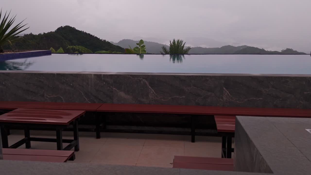 Aerial drone reveal shot starting from a blue infinity pool surface tilting up to a foggy mountain range. Scenic resort view in the highlands of Davao Philippines with tropical plants
