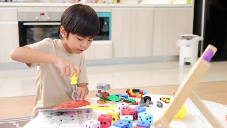 A young boy intently assembles colorful toys on a table in a bright, modern kitchen setting