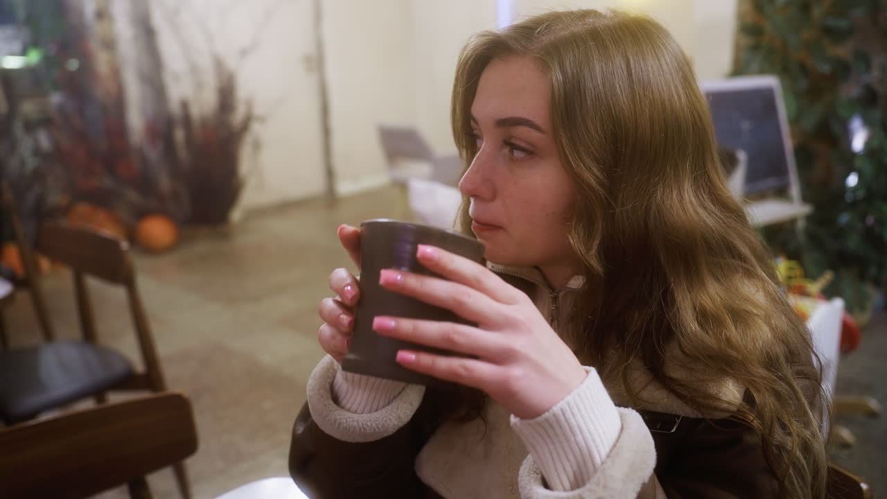 Calm girl in brown shearling jacket sipping coffee, immersed in cozy cafe ambiance. Soft lighting enhances peaceful moment, creating a relaxing and intimate atmosphere, perfect for relaxation