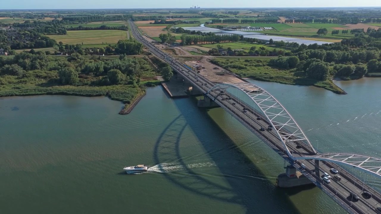 Vista aerea di un motoscafo che passa sotto un grande ponte ad arco.