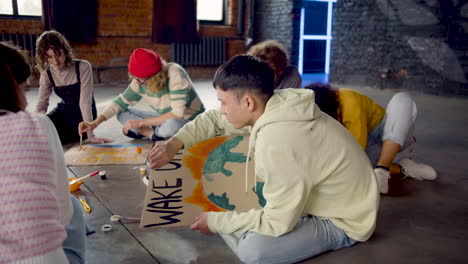 jóvenes activistas ambientales pintando carteles sentados en el suelo