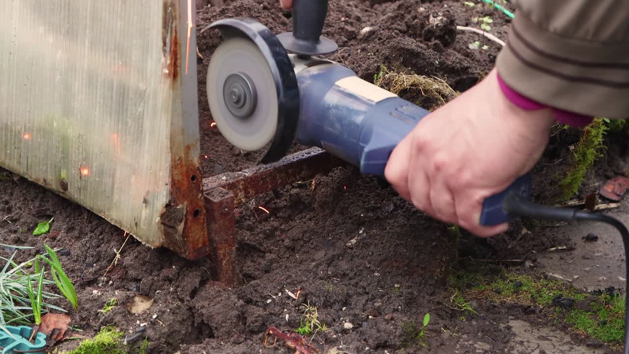 Close-up of a man with an angle grinder cutting a rusty metal greenhouse.