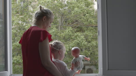 Mamá-Con-Hija-Tomando-El-Aire-En-Una-Ventana-Abierta-Durante-El-Aislamiento-Del-Coronavirus