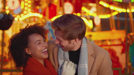 portrait of couple enjoying on date in standing by carousel at christmas funfair at night - shot in slow motion