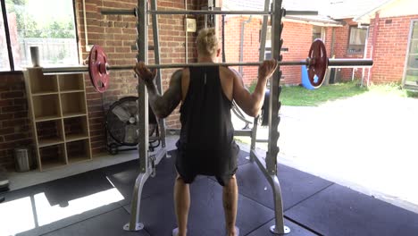 Tattoo-man-muscles-in-home-gym-barbell-squat-from-behind