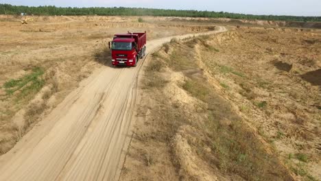 red dump truck driving on a dirt road in a quarry