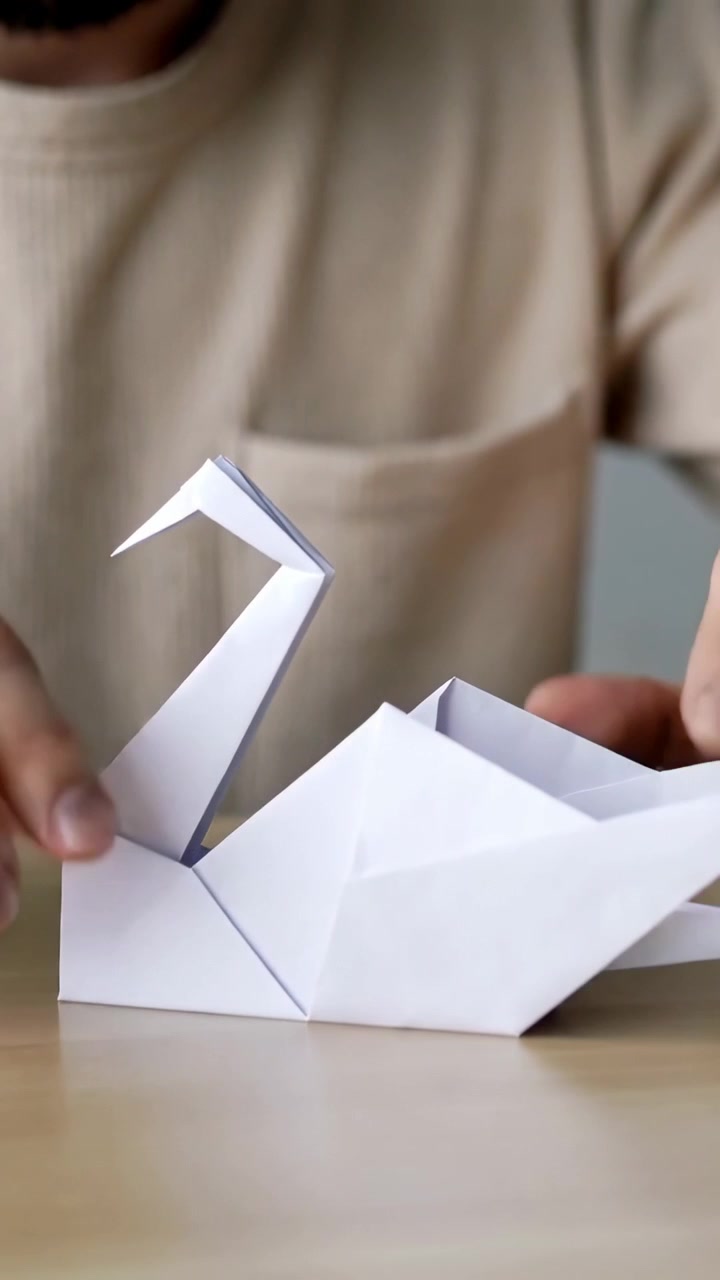 Video verticale: Mani maschili che si protendono piegando un cigno di carta bianco su un tavolo di legno, finendo il cigno