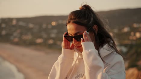 hermosa mujer modelo joven con capucha, gafas de sol posa para la cámara en la luz dorada del sol durante el amanecer del atardecer