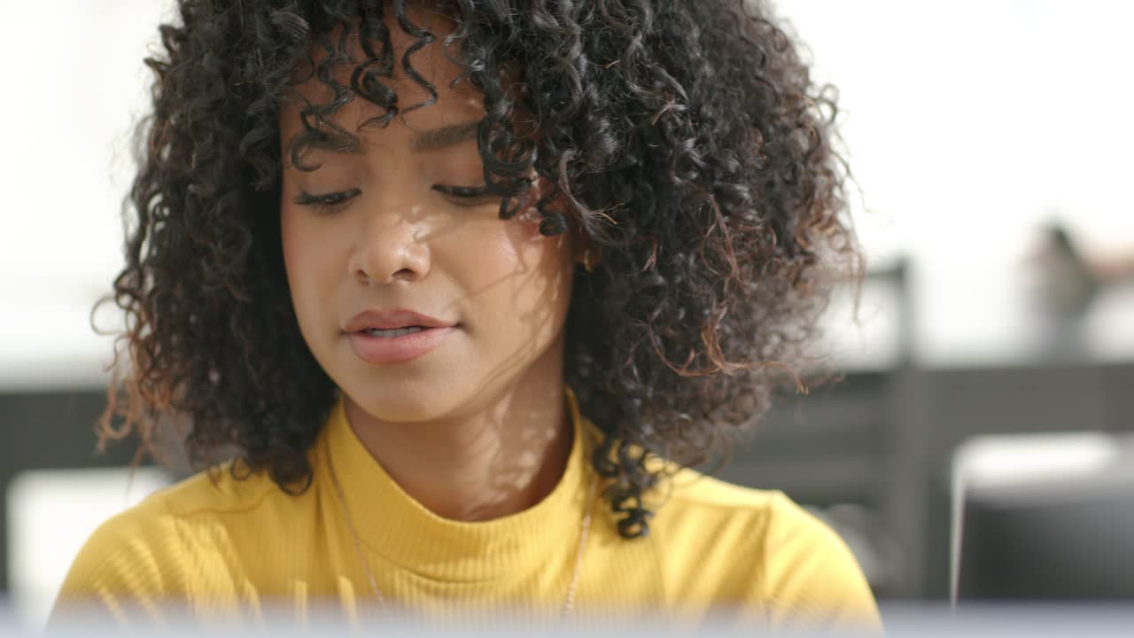 Adult female in yellow turtleneck reading from monitor at desk, mouthing replies while thinking