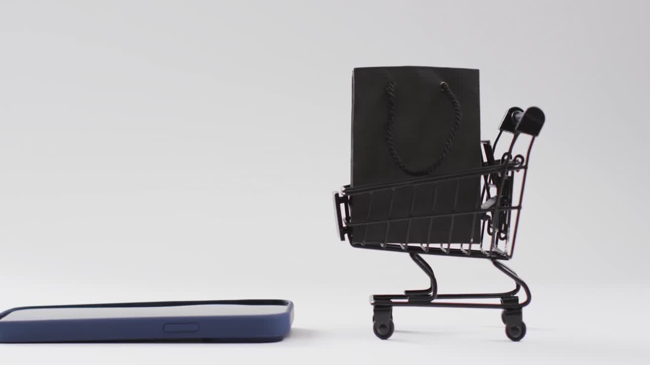 Video of smartphone, shopping bag and trolley with copy space on white background