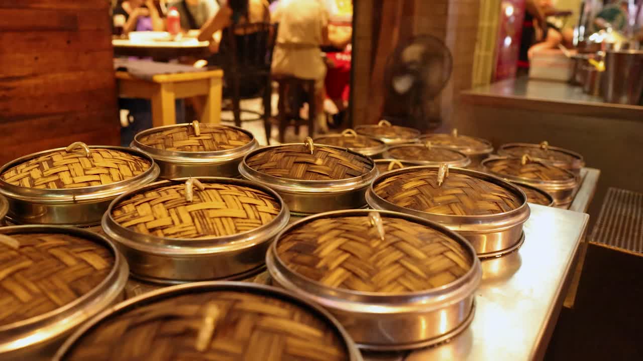 Multiple bamboo steamers on metal counter, warm lighting, shallow depth, bustling Chinatown street food scene