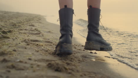 las piernas de una mujer en primer plano bailando en una playa de arena. las piernas de una chica con botas elegantes.