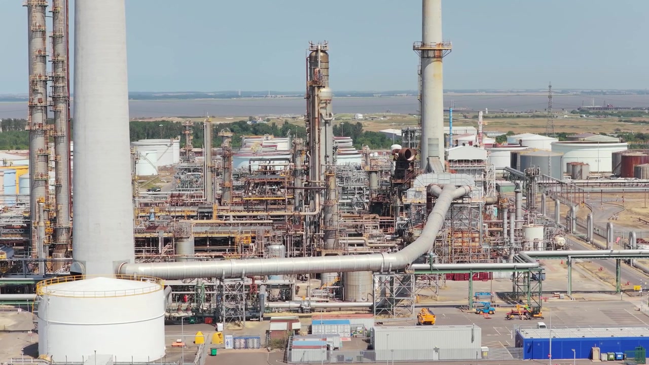 Grande instalação industrial com altas torres de metal e tubulações de conexão durante um dia claro perto do Estuário do Humber na Inglaterra, onde as operações de processamento ocorrem ao ar livre sob céus azuis claros