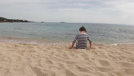 a young brunette girl playing with the sand wearing a striped dress on a sandy beach