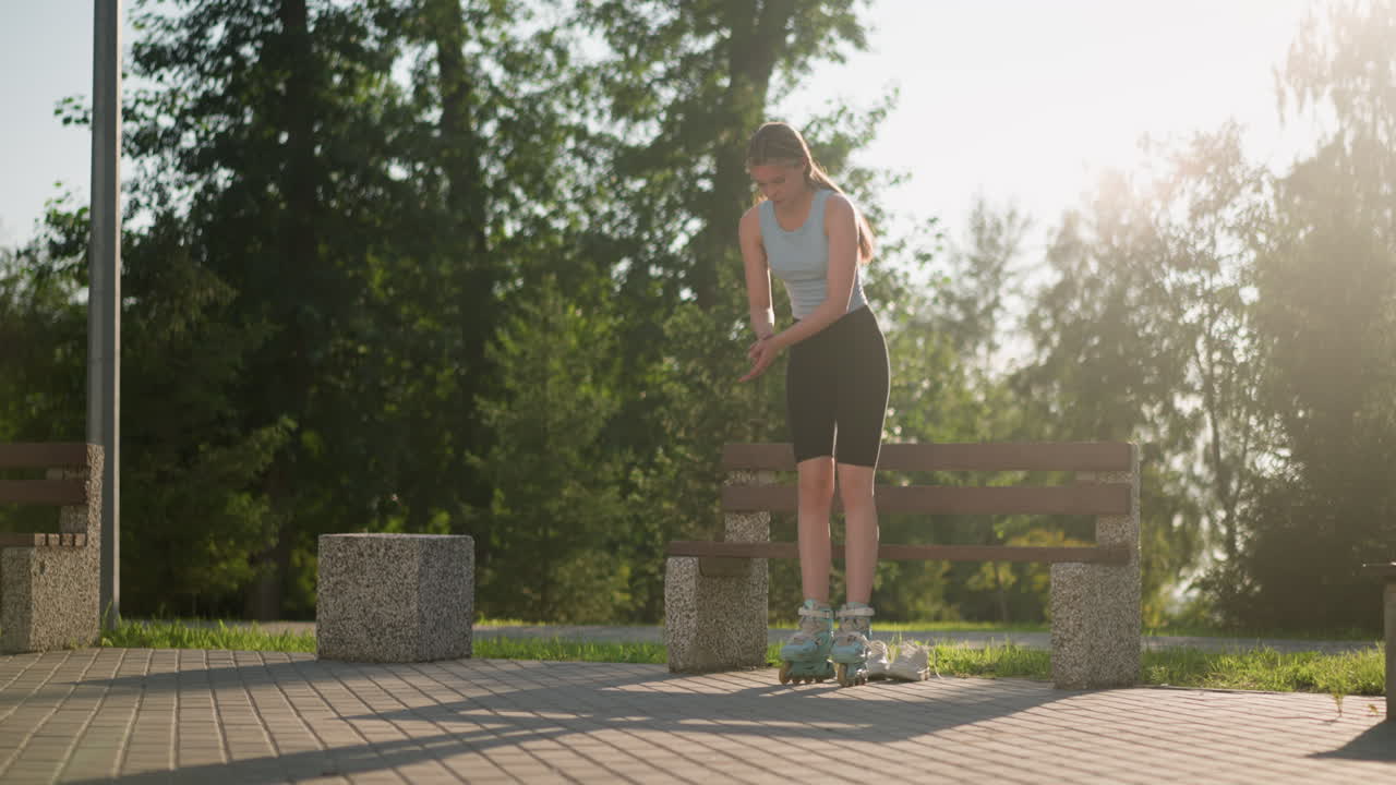 joven tratando de equilibrarse mientras se levanta del banco mientras usa patines en el parque, con zapatillas blancas debajo del banco y la luz del sol iluminando los árboles verdes en el fondo