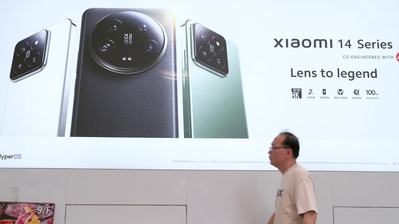 Pedestrians walking past a commercial advertisement from the Chinese tech brand Xiaomi showcasing the Xiaomi 14 Series smartphone outside the official flagship store.