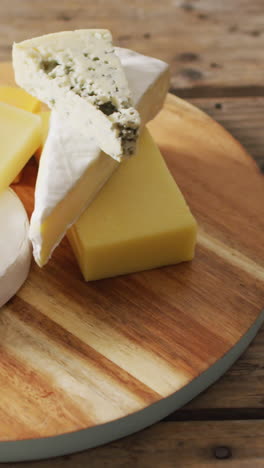 video of assorted hard and soft cheeses on wooden chopping board and rustic table, with copy space