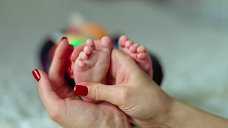 mother's hand holds her babe's foot and rubs it with her thumb. baby boy lies on the bed with white plaid. blurred backdrop.