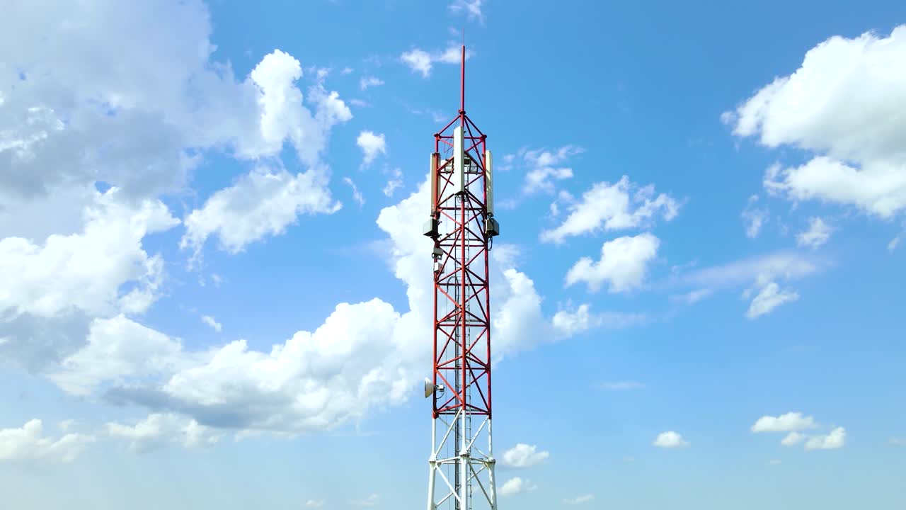torre de red de telefonía celular con antenas 5g en rojo y blanco con cielo azul y nubes blancas en el fondo