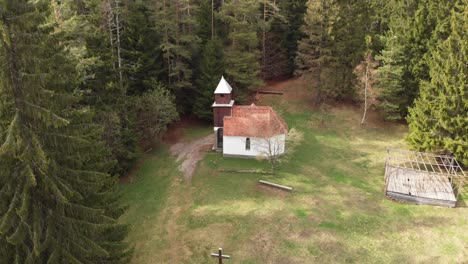 Toma-Aérea-De-Una-Antigua-Iglesia-En-Medio-De-Un-Bosque-De-Pinos-En-Las-Montañas-De-Los-Cárpatos,-Rumania