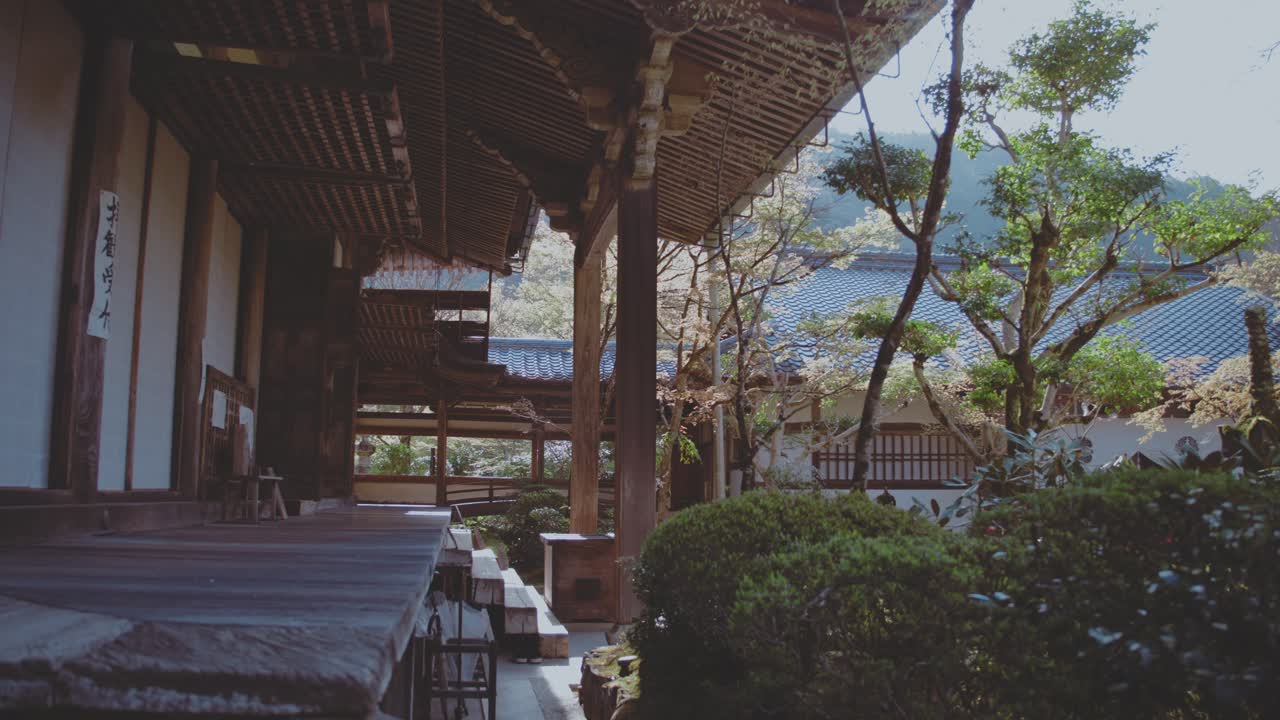 Serene view of a traditional Japanese temple surrounded by lush greenery in Takaosan, Japan. The peaceful architecture blends harmoniously with the natural landscape under a clear sky.