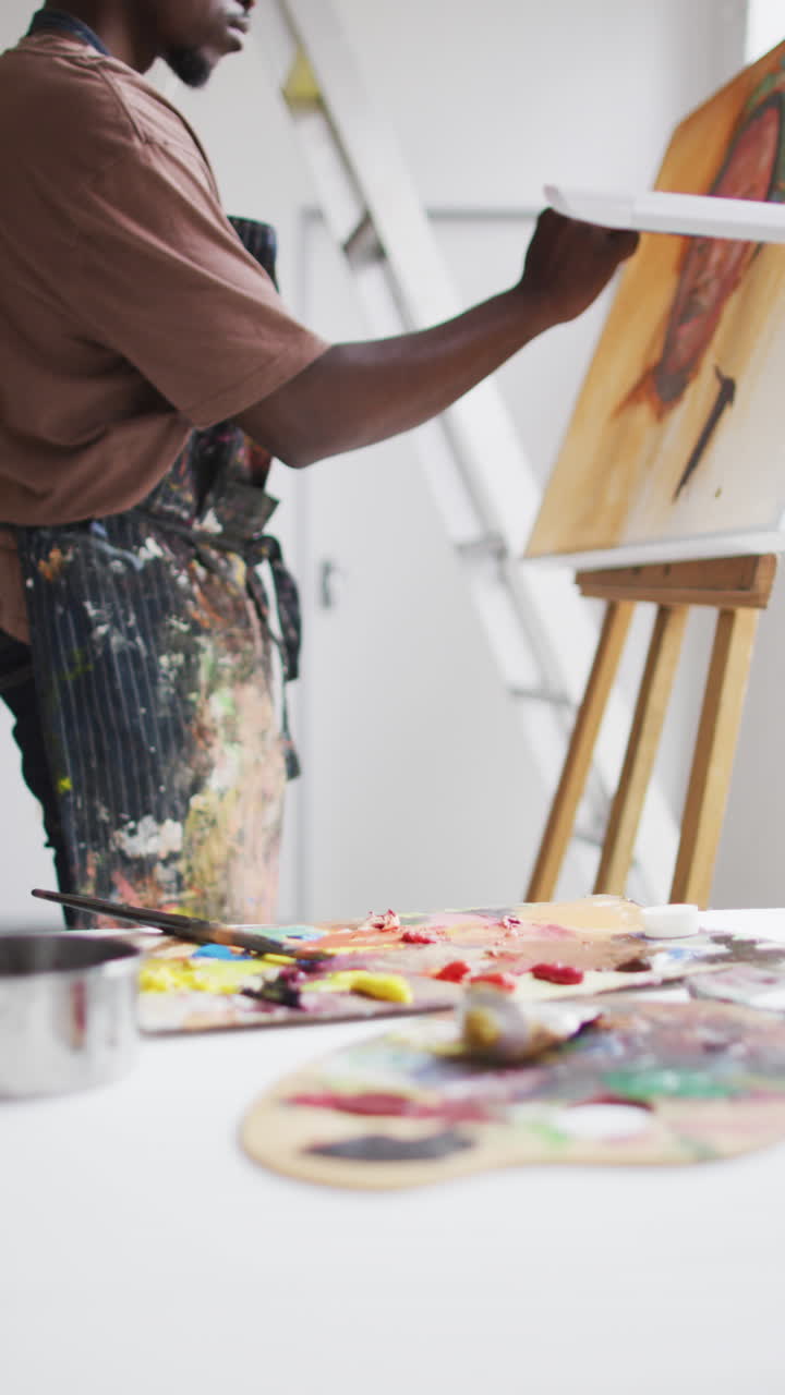 African American artist paints a portrait in studio, wearing headphones