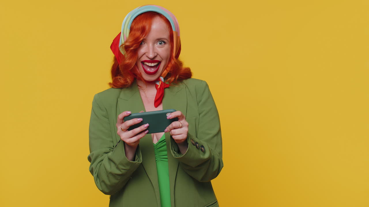 preocupada, graciosa, adicta, pelirroja, jugando con entusiasmo a un videojuego de carreras en su teléfono móvil.