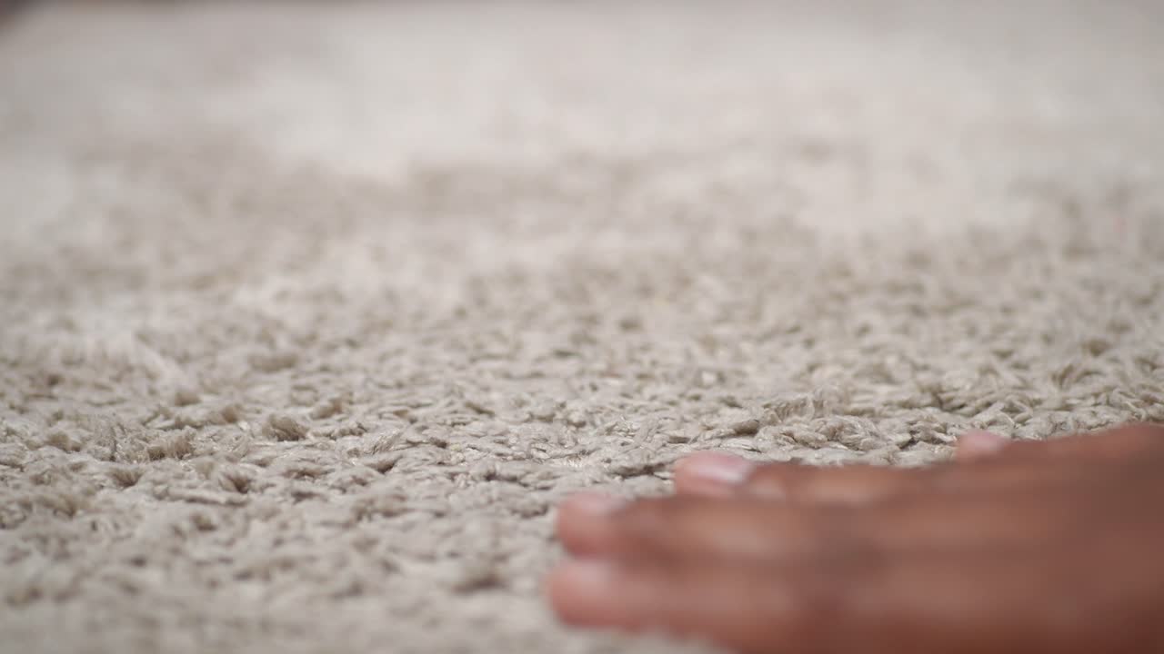 Primo piano della mano di una persona che tocca un soffice tappeto beige