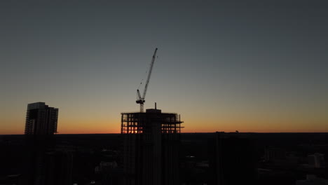 aerial shot of silhouette of crane building apartments and offices on a construction site at sunset