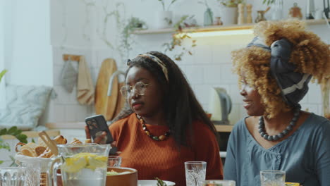 two young black women sitting at dinner table and taking selfie with phone
