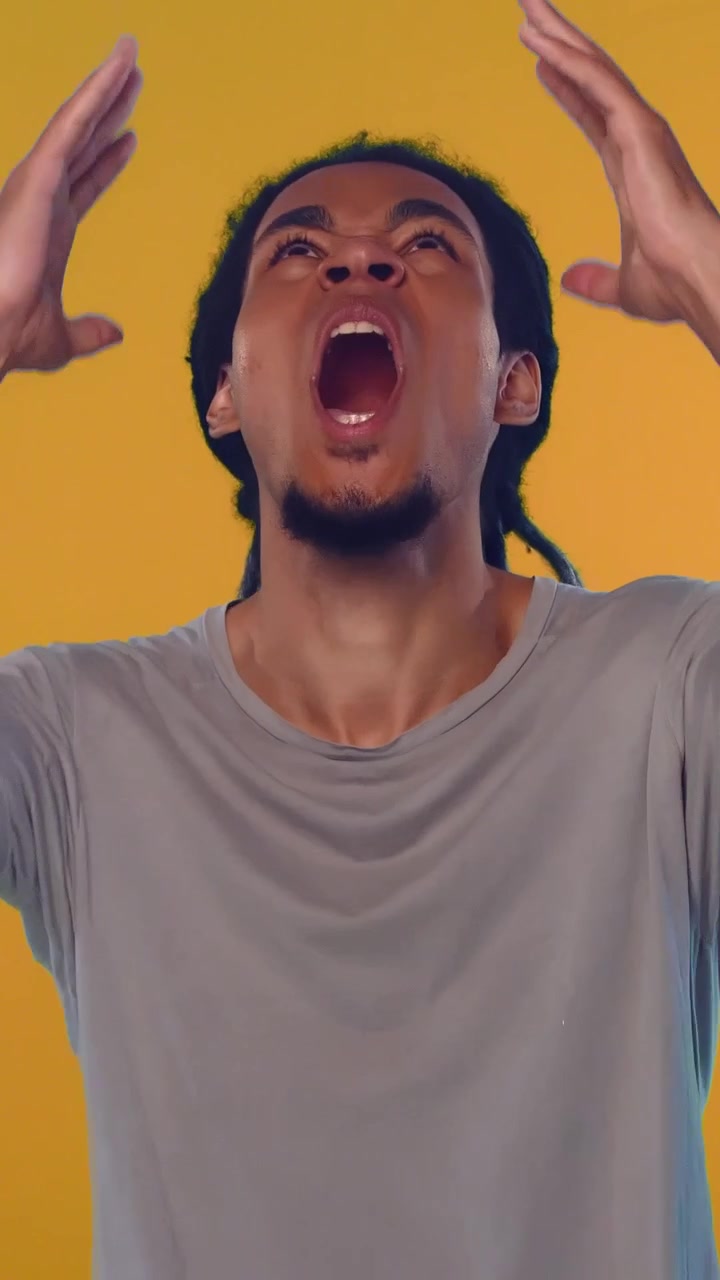 Angry african american man with dreadlocks gesturing and screaming on yellow