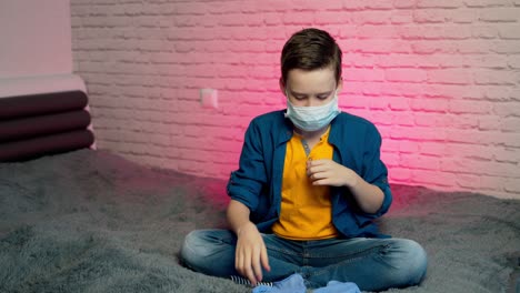 beautiful boy in self isolation during covid-19 pandemic. child puts on face medical mask