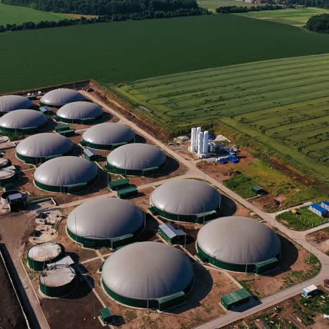 beautiful scenery of the field containing biogas plant. flying over the round biogas storages. forests and village houses at the backdrop