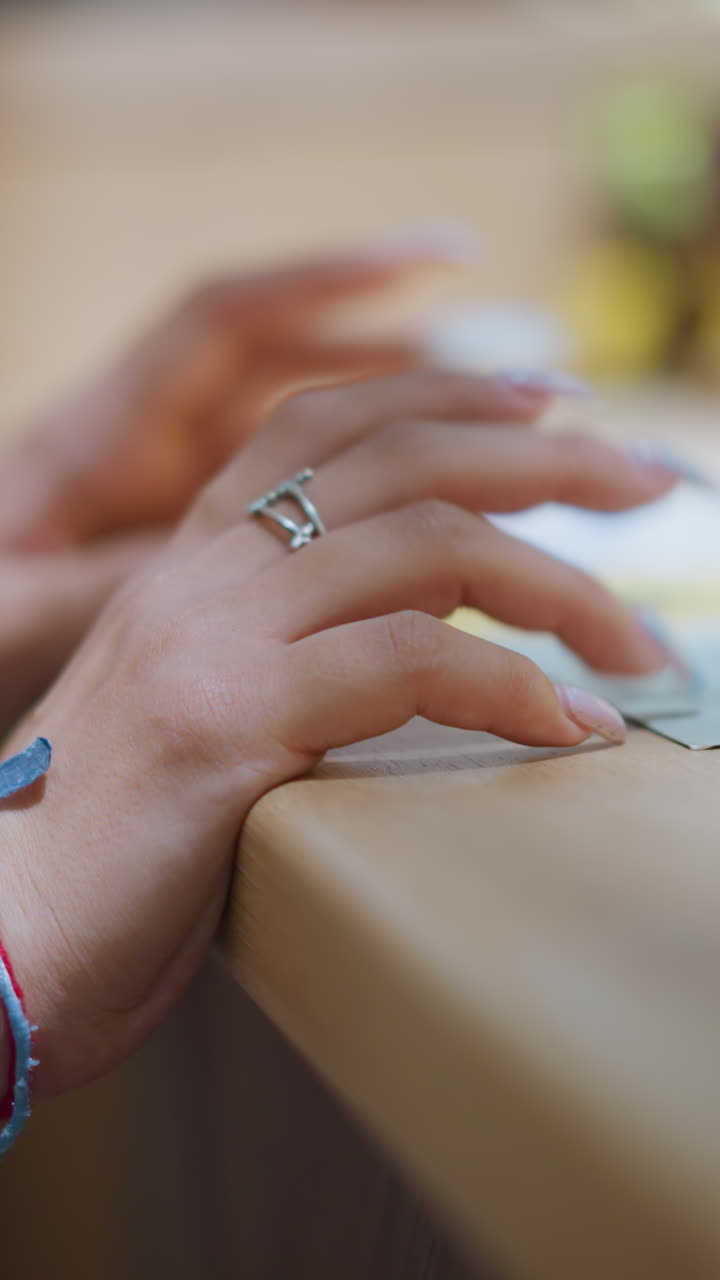 은색 팔와 은색 으로 장식된 여성의 손, 테이블 위에 있는 종이 위에 부드럽게 누워있는 은 손, 은 흐릿한 배경과 함께 성찰이나 의사 결정을 암시합니다.