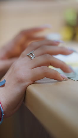 primer plano de las manos de la mujer adornadas con una pulsera de plata y un cordón rojo, uñas pulidas descansando suavemente sobre el papel en la mesa, sugiriendo contemplación o toma de decisiones, con un fondo suave y borroso