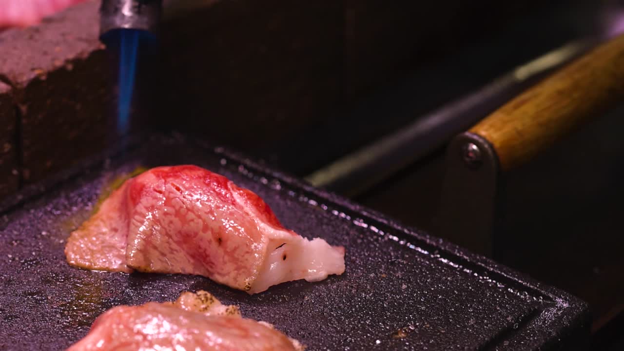 Watch a steak being seared with a blowtorch on a grill, highlighting the sizzling and browning process.