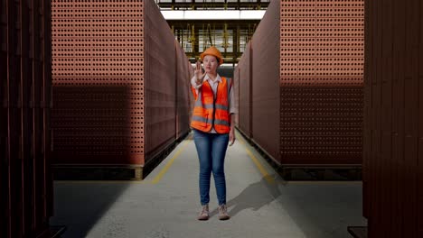 full body of asian female engineer with safety helmet disapproving with no hand sign while standing with red brick packed in stacks are stored