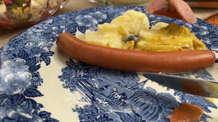 Nærbillede af spisning af typisk tysk bockwurstpølse og hjemmelavet kartoffelsalat fra et personligt perspektiv.