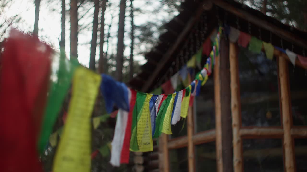 Bandiere di preghiera buddiste colorate che sventolano davanti a una rustica baita in legno nella foresta dell'Altai. Atmosfera spirituale e pacifica.