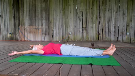 Elderly-senior-gray-haired-woman-in-savasana-stretching-on-a-mat-with-coffee-cup-nearby