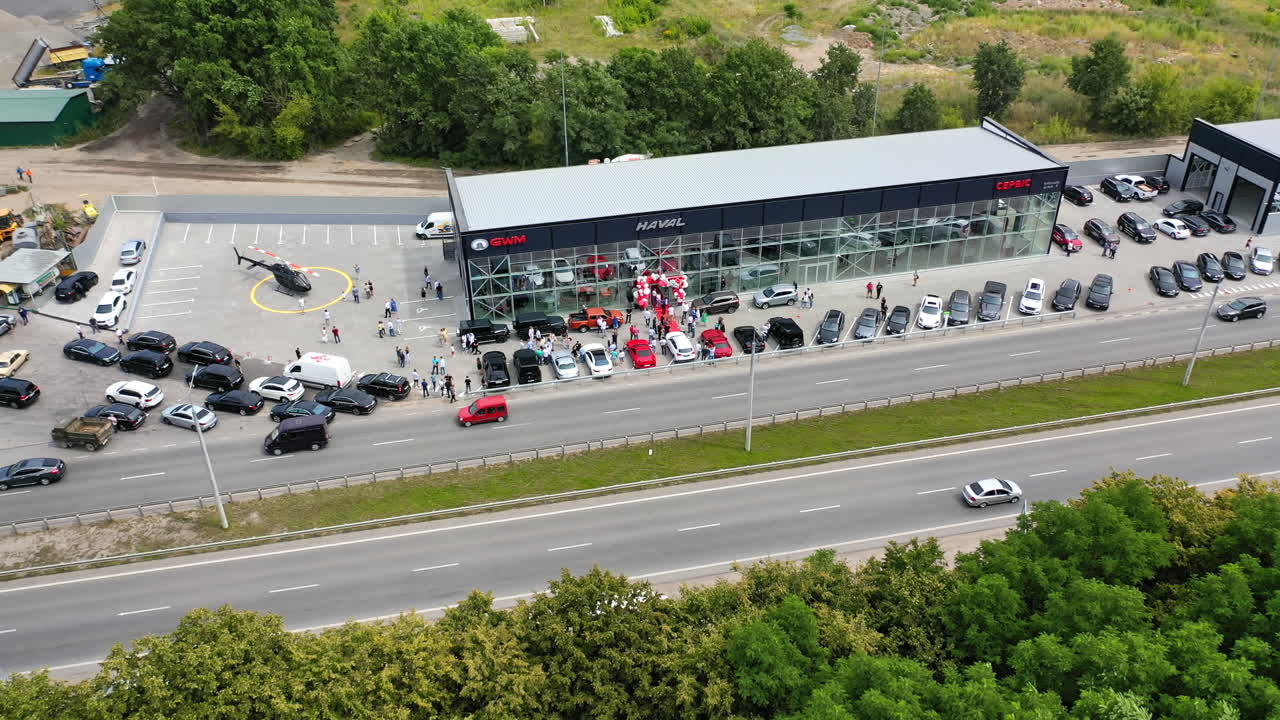 Motorway going along the new car dealership. People look at multiple autos and helicopter near the centre.