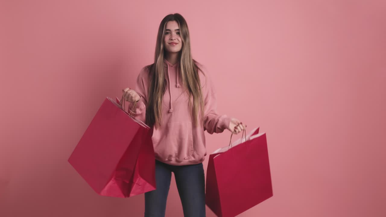 Happy shopaholic woman with shopping bags in pink studio