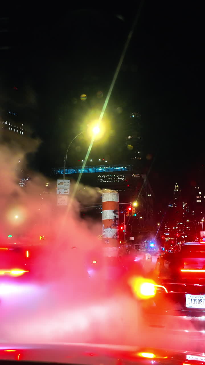 New York, USA, 1 April 2026: Night traffic in New York City with steam rising from street. Steam rising from manhole on busy Manhattan street at night with red car taillights and city lights