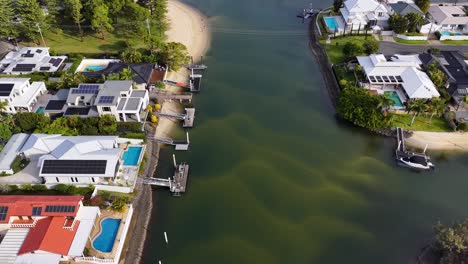 drone camera glides above upscale riverside houses with private pools, docks, and lush landscaping, following a gentle river curve under bright daylight