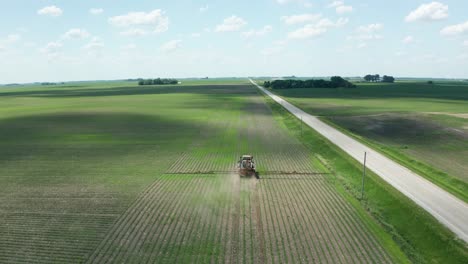 aerial, tractor spraying pesticide on crops in rural agricultural farm field