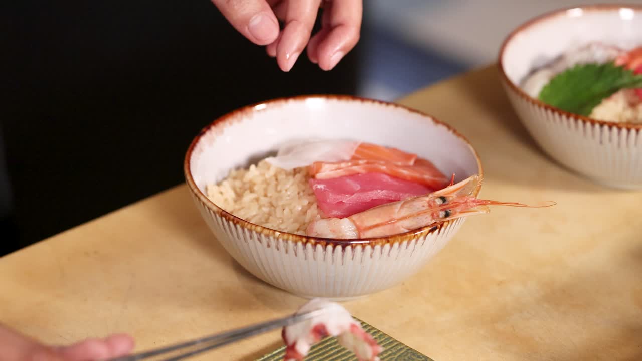 Close-up de um chef usando hashis para dispor salmão, atum e camarões sobre o arroz